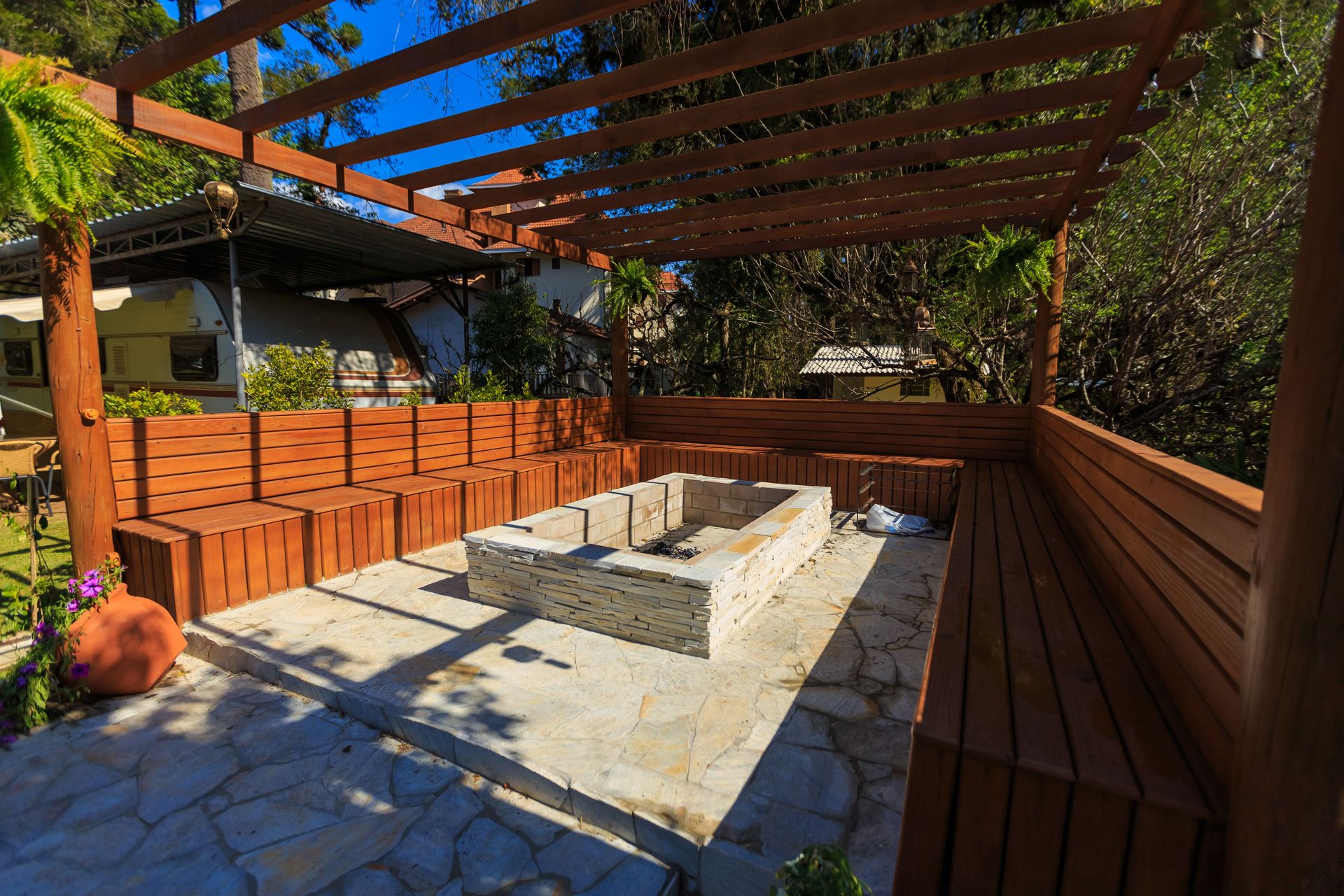 Inviting patio with a stone fire pit and wooden benches under a pergola, perfect for outdoor relaxation.