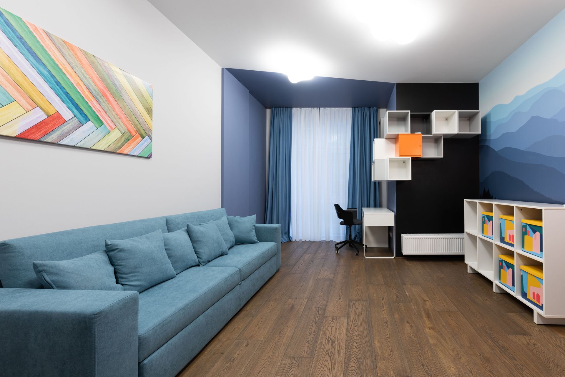 Contemporary living room featuring a blue couch, abstract art, and functional workspace.